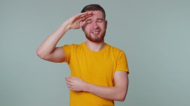 Sarı tişörtlü sakallı genç adam baş ağrısı problemini tedavi etmek için tapınakları ovuyor, tansiyon, migain, stres, ekşitme, acı içinde yüzme, yüksek tansiyon gri arka planda tek başına izole edilmiş.