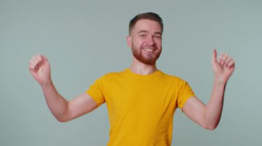 Sarı tişörtlü yakışıklı adam bağırıyor, el kol hareketi yapıyor başarıyı, galibiyeti ve gol atanları kutluyordum. Gri stüdyo arka planında genç yetişkin bir çocuk var.