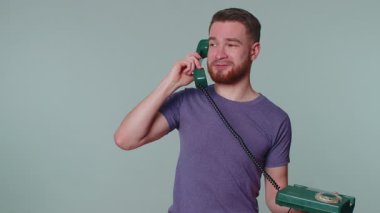 Hey sen, beni ara. Mor tişörtlü neşeli sekreter 80 'lerin telli klasik telefonundan konuşuyor ve beni geri ara diyor. Gri stüdyo arka planında yalnız poz veren genç bir adam.