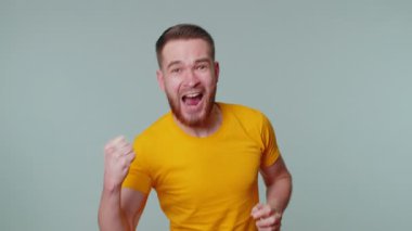 Sarı tişörtlü yakışıklı adam bağırıyor, el kol hareketi yapıyor başarıyı, galibiyeti ve gol atanları kutluyordum. Gri stüdyo arka planında genç yetişkin bir çocuk var.
