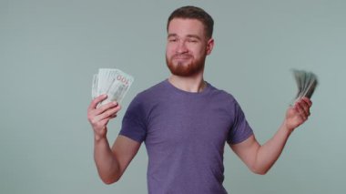 Mor tişörtlü kibirli zengin adam elinde nakit para, banknotlar, gülümsüyor ve kameraya bakıyor. Gri stüdyo arka planında izole edilmiş. Gelir, kredi, borç, tasarruf kavramı
