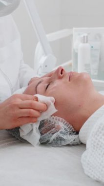 Kozmetik doktoru kadın yüzü, spa salonundaki pamuklu mendillerle boynu temizliyor. Kız teninin kozmetik güzellik prosedüründen önce temizlenmesi. Güzellik uzmanından yüz bakımı. Dikey yakın plan portre