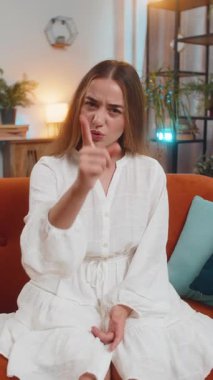 Evdeki kanepede oturan öfkeli genç beyaz kadın, kızgın bir şekilde seni kameradan işaret ediyor, hoşnutsuz ve öfkeliydi. Yetişkin kız ciddi şekilde suçlanıyor, üzgün ve patlamaya hazır. Dikey.