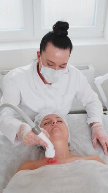 Güzellik uzmanı kadın RF kaldırma prosedürü yapıyor. Yüz ve göğüs, kolajen maskesi. Kozmetik uzmanı vakum masaj terapisi için elektrikli ekipman kullanıyor. Cilt bakımı, güzellik tedavisi. Dikey