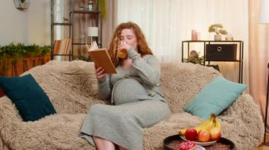 Hamile genç bir kadın evde kanepede oturmuş taze portakal suyu yudumluyor ve rahat bir ifadeyle hamilelik kitabı okuyor. Geleceğin anneliğini ve nazik yaşam tarzını yansıtan mutlu anları seven bir kız.