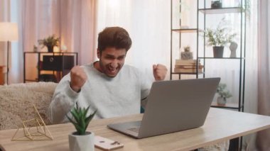 Genç Hintli adam dizüstü bilgisayar kullanıyor, e-postaları kontrol ediyor, beklenmedik bir şekilde önemli bir mektup alıyor, zaferi kutluyor. İspanyol adam sevinçle gülümsüyor, sevinçle el kaldırıyor, iyi haberlerle heyecanlanıyor..