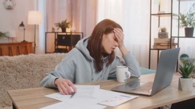 Yorgun, tembel ve serbest çalışan genç bir kadın kanepenin üstündeki dizüstü bilgisayarda çalışıyor. Günün sonunda tek eliyle başını tutarak yorgun görünüyor. Evraklar, bir fincan kahve masada. Evden çalışan kız..