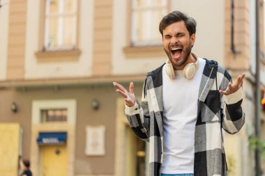 Hintli genç adam bağırıyor stres yüzünden bağırıyor korku, umutsuzluk panik, sürpriz şok, öfke belirtileri hissediyor. Şehir caddesinde duran sinirli İspanyol adam..