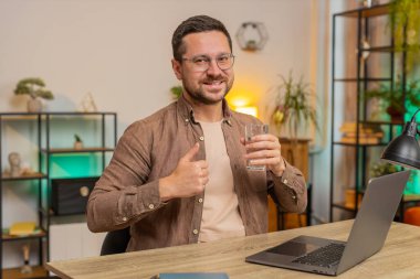 Ofis odasında dizüstü bilgisayarla çalışırken masa başında oturmuş su içen Kafkasyalı bir iş adamı. Genç erkek serbest çalışan adam bilgisayar ekranı internette geziniyor..