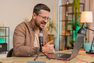 Mutlu heyecanlı blogger adam podcast yapıyor, atölye veriyor, webinar yapıyor. Genç Kafkasyalı nüfuzlu adam mikrofon ve dizüstü bilgisayara konuşuyor, video görüşmesi yapıyor, merkez ofiste tartışıyor..