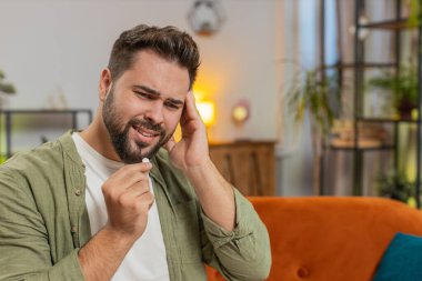 Baş ağrısı çeken bir adam oturma odasında ilaç, sağlık ve tedavi görüyor. Erkek hasta ilaç, anksiyete ya da su, ilaç ya da hastalığın tedavisi.