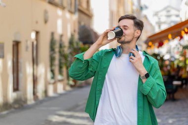 Yakışıklı beyaz adam sabah kahvesinin tadını çıkarıyor sıcak içecek ve gülümsüyor. Dinleniyorum, ara veriyorum. Şehir merkezi caddesinde yürüyen mutlu genç bir adam, gitmek için kahve içiyor. Dışarıdaki kasaba yaşam tarzları.