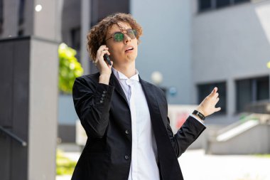 Stresli Kafkasyalı işadamı sinirli konuşmalar hayal kırıklığına uğramış cep telefonu konuşmaları şehir merkezindeki iş anlaşmazlığını sona erdirdi. Güneş gözlüklü, takım elbiseli, kıvırcık saçlı üzgün genç adam..