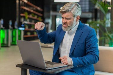 Takım elbiseli kızgın yetişkin patron, ofiste modern işyerinde otururken bilgisayarla video görüşmesi yapıyor. Tatminsiz iş adamı yöneticileri, şirketlerin sorunları hakkında astlarıyla iletişim kuruyor..