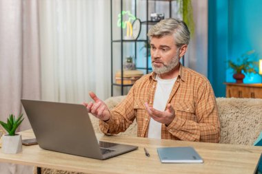 Beyaz, olgun bir adam önemli bir iş kamerası görüşmesi yapmak için dizüstü bilgisayar kullanıyor. Adam ciddi odaklanmış görünüyor, tartışma sırasında aktif hareket ediyor, internetten video görüşmesi.