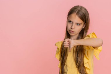 Genç kızın kaşlarını çatması, açıkça hayal kırıklığını, reddedilmeyi ve hayal kırıklığını ifade eden bir jest gösteriyor. Pembe arka planda izole edilmiş okul çocuğu güçlü negatif duyguyu özgüvenle tasvir ediyor.