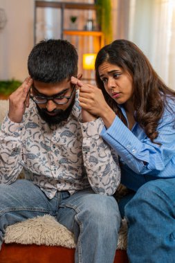 Hintli çift erkek kanepesinde oturuyor, erkek üzgün görünüyor kız ona duygusal destek ve rahatlıkla sarılıyor. Genç aile şefkat, ilgi ve derin bağları paylaşıyor.