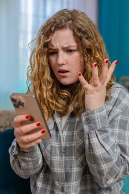 Evde sinirli bir şekilde cep telefonundan mesaj atan genç bir kadın, kızgınlıkla ve hayal kırıklığıyla mesaj yolluyor. Kanepede oturan beyaz saçlı kız el sallıyor, tatminsizliğin duygusal ifadesi.