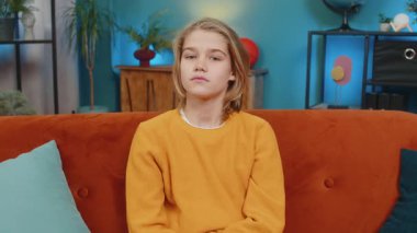 Kafkasyalı genç çocuk evde samimi bir gülümsemeyle bir portre için poz veriyor, rahatlatıcı. Kollarını kavuşturup koltukta rahatça oturur, kameraya bakar, mutluluk ve kendine güvenini gösterir.