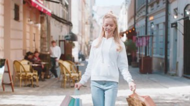 Alışveriş merkezinde alışveriş yaptıktan sonra açık havada hediyelerle dolu poşetlerle gülümseyen esmer, genç bir kadın tüketici. Şehir caddesinde yürüyen genç turist kız. Kasaba yaşam tarzları.
