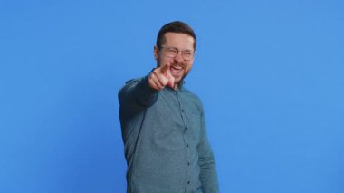 Hey sen! Gözlüklü, mutlu, beyaz bir genç adam kameraya bakıp, şanslı bir oyun kazananı seçiyor. Bu da sana harika bir terfi olduğunu gösteriyor. Mavi arkaplanda izole edilmiş adam