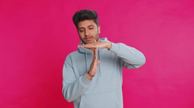Ciddi şekilde üzgün Hintli genç adam mola verme hareketi yapıyor, sınır veya dur işareti, baskı yok, daha fazla zamana ihtiyacım var, dinlenin, dinlenin, yardım edin. Pembe stüdyo geçmişinde izole edilmiş Arap bir adam.