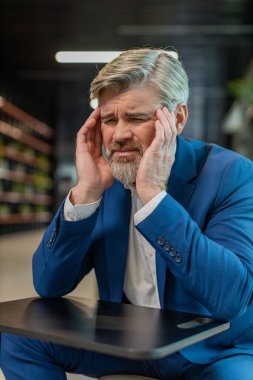 Baş ağrısı, tansiyon, migren ve modern ofis lobisindeki stresten muzdarip orta yaşlı hasta işadamı. Otel koridorunda oturan yakışıklı, serbest çalışan bir iş adamı. Fazla çalışma.