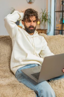 Evdeki kanepede oturan üzgün genç Hintli adam dizüstü bilgisayar kullanıyor ve stres altında. Sakallı adam kayıplara tepki veriyor. Oturma odasındaki internet sitesinde kötü haberler. Bilgisayar virüsü.