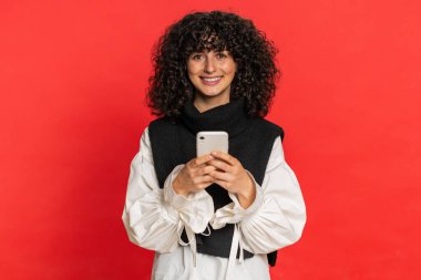 Beyaz bir kadının mesajlaşması akıllı telefon sosyal medya uygulamalarında içerik paylaşımı, rahatlama filmi izlemesi. Genç kız kırmızı arka planda izole edilmiş cep telefonu gülümsemesi kullanıyor.