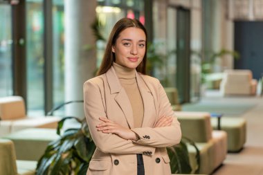 Kendine güvenen, resmi giyinmiş, kameraya bakan kadın patron. Güzel kadın ofis çalışanı modern ofis lobisinde mutlu ve kollarını kavuşturmuş duruyor. İş adamları portreleri