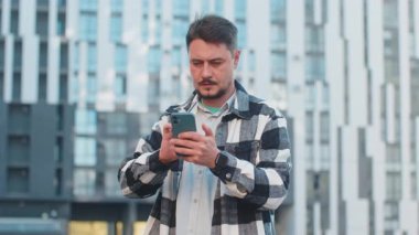 Beyaz, olgun bir adam kredi kartı ve akıllı telefon kullanarak internetten alışveriş siparişleri alıyor ve internetten yemek sipariş ediyor. Şehir merkezinde binanın karşısında duran adam.