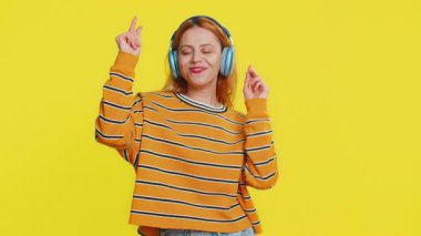 Bluz giymiş neşeli beyaz kadın kulaklıkla müzik dinliyor ve diskoda dans ediyor. Eğlenceli, jestli eller yapıyor. Sarı arka planda izole edilmiş genç bir kız.
