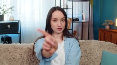 Evdeki genç kadın kanepeye oturmuş anlaşmazlık jestleriyle parmağını sallıyor ve açıkça hayır diyor. Kafkasyalı kız memnuniyetsiz ve mutsuz, reddediyor, sinirleniyor ve olumsuz duygular besliyor..