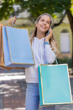 Mutlu beyaz kadın turist kızın portresi gülümsüyor. Elinde alışveriş paketleri olan caddede gülüyor. Telefonda konuşuyor..