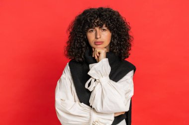 Beyaz, kıvırcık saçlı, yorgun, ilgisiz ifadelerden sıkılmış, sıkıcı hikayelerden bıkmış, iletişim konuşmalarıyla ilgilenmeyen, hoşnutsuzlukla ilgilenmeyen, ilginç olmayan genç bir kadın. Kırmızı arkaplanda izole edilmiş kız