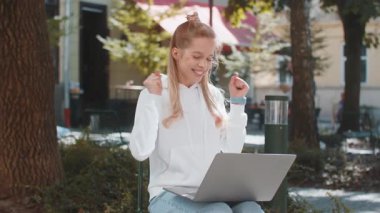 Dizüstü bilgisayarla çalışan mutlu Kafkasyalı kadın zafer çığlıkları atarak iyi haber başarısını kutluyor kumarhane piyango parası ikramiyesi zaferini kazanıyor. Şehir caddesinde heyecanlı bir genç kız.