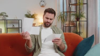 Stresli esmer adam oturma odasında ödenmemiş banka borçlarına bakıyor evrak işleri, planlama bütçesi ipotek ödemelerini hesaplıyor, son teslim tarihini hesaplıyor. Adam eve kağıt para atıyor..