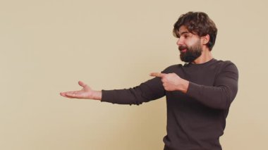 Lübnanlı genç adam onaylıyor ve boş bir yeri işaret ediyor. Ticari metinler için reklam alanı, ürün tanıtım logosu için kopyalama alanı. Latin Hintli adam bej renkli stüdyo arka planında izole edilmiş..