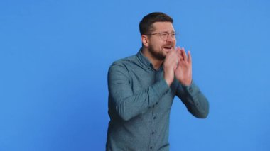 Ağız kenarında el ele tutuşan orta yaşlı, etkileyici beyaz adam bağırıyor, bağırıyor, bağırıyor, indirim duyurusu yapıyor. Mavi arkaplanda izole edilmiş adam