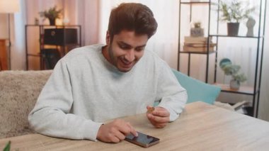 Bitcoin 'li genç Hintli adam akıllı telefon uygulamasındaki kripto döviz çizelgelerini kontrol ediyor yaklaşık karı hesaplıyor ve kameraya BTC' nin kazandığını gösteriyor. İspanyol adam evde tatmin olmuş görünüyor.