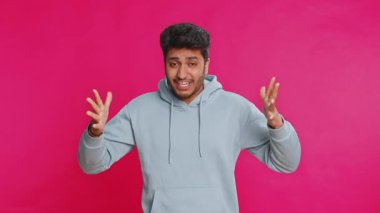 Kapüşonlu Arap genç adam stres yüzünden bağırıyor. Sorunlar, umutsuzluk, panik şaşkınlığı hissediyor. Panik şoku, öfkeyi ifade ediyor. Hintli adam pembe stüdyoda tek başına izole edilmiş.