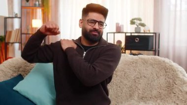 Evde oturan Hintli adam gerilimle omuz omuza oturuyor, kanepede otururken yüzünde acı gösteriyor. Arap adam, kas ya da eklem gerginliğinden kaynaklanan rahatsızlığı hafifletmek için ağrıya sessizce tepki verir.