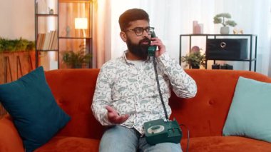 Hintli genç adam evinde kanepede oturuyor ve yorgun yüzüyle eski moda 90 'ların telefonuna cevap veriyor, dolandırıcılık ya da kötü haber alıyor. Arap adam telefon tutarken sıkılmış, sinirlenmiş ve hayal kırıklığına uğramış görünüyor.