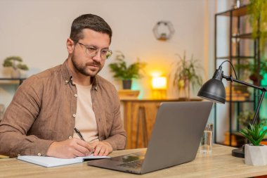 İnternetteki video dersine ya da ofis bilgisayarındaki laptop toplantısına katılırken not alan ya da not alan genç iş adamı. Webcam 'e bakan Serbest Çalışan Destek Servisi.