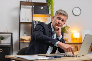 Takım elbiseli bir işadamı, ofis masasında önemli bir yaratıcı proje çalışma fikri düşünüyor. Kendine güvenen yönetici serbest çalışan adam laptopta çözümler aramakla meşgul.