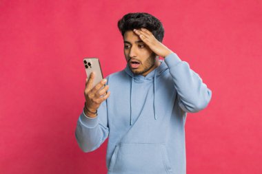 Üzgün Hintli adam akıllı telefon daktilo kullanıyor, oyun oynuyor, kaybediyor, piyango aniden şaşırıyor kötü şans kaybı şanssız haber. Kızıl arka planda izole edilmiş Arap Hindu sakallı adam.