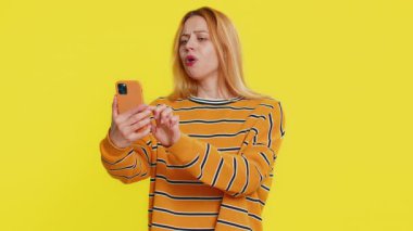 Üzgün beyaz kadın akıllı telefon daktilo kullanıyor, oyun oynuyor, aniden piyango sonucuna şaşırıyor kötü şans kaybı şanssız haber. Sarı arka planda izole edilmiş mutsuz, çekici kız.