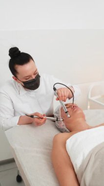 Kozmetik bilimci mikro akım cihazı terapisini uygularken beyaz kız kanepede yatıyor. Genç bir kadın modern kozmetik kliniğinde gençleştirme için anti-yaş cilt terapisinden hoşlanıyor..