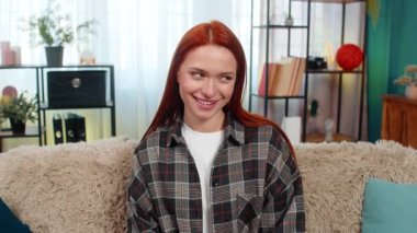 Genç bir kadın kameraya göz kırpıyor. Cilveli bir gülümsemeyle kendine güveni ve cazibesini gösteriyor. Kafkasyalı kızıl saçlı kız kanepenin üzerinde eğleniyor, duygularını ve kişisel çekiciliğini ifade ediyor.