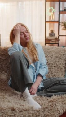 Evde alnını ovuşturan genç bir kadın, şiddetli baş ağrısından dolayı baskı ve rahatsızlık hissediyor. Kanepede uzanmış, gün batımında enerjiyi emen migrenle boğuşan bir kız.